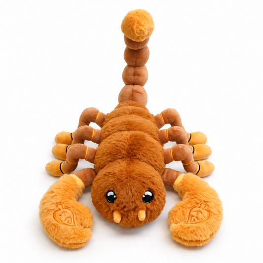 A plush toy scorpion in shades of orange and brown, featuring embroidered eyes and small teeth, photographed on a clean white background.